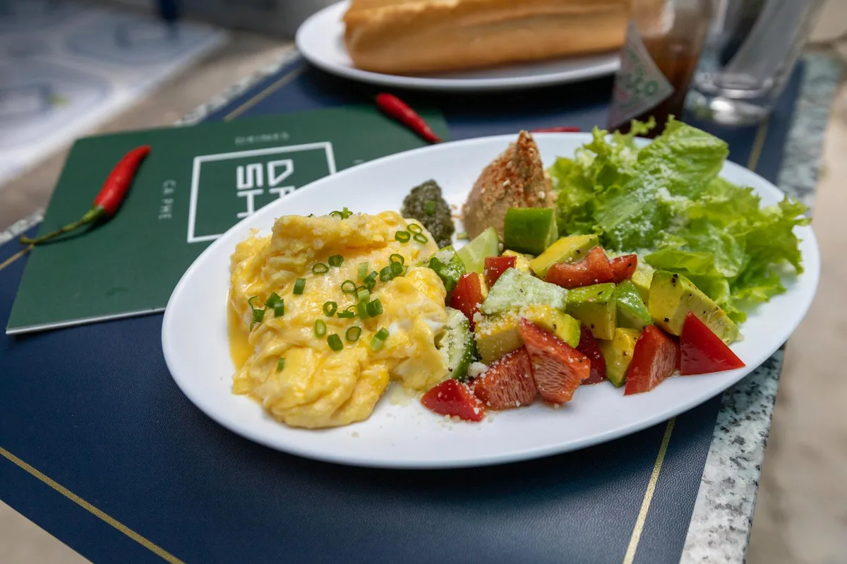 Scrumptious breakfast featuring scrambled eggs, fresh salad, and a baguette on a white plate.