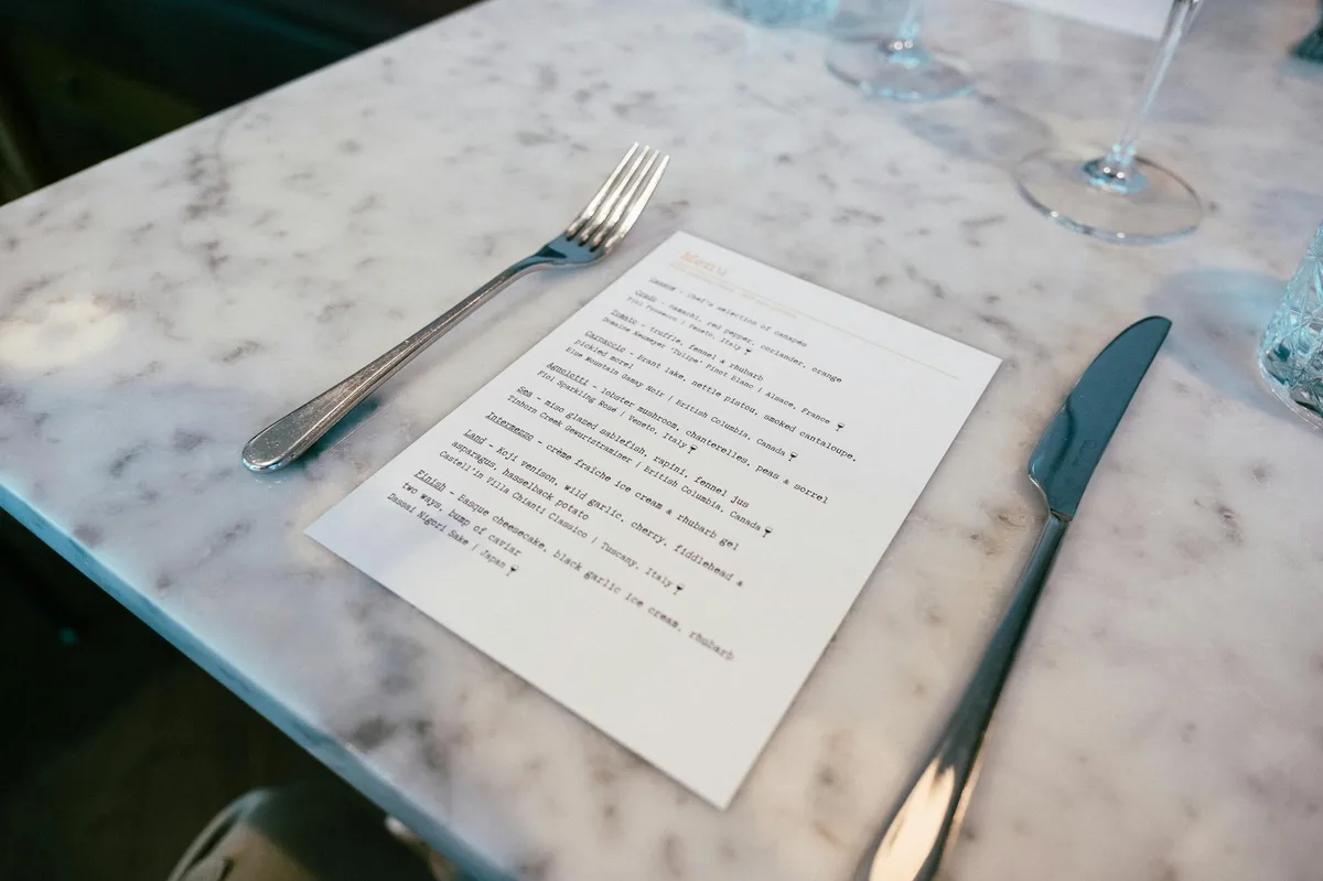 A marble table setting in an upscale restaurant featuring a menu, fork, and knife, offering a taste of fine dining.
